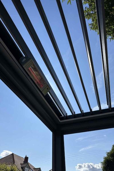 Close-up of the Deluxe Anthracite Grey metal Pergola's open louvres, framing a backdrop of trees and blue skies, available in 5x3.***Image for illustrative purposes only - displaying a 3x3 model*
