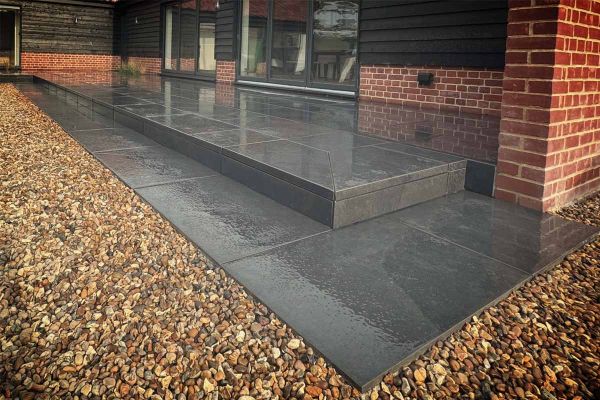 Side view of corner of small florence dark patio shown in the wet, with one garden step up showing downstand edges.***Willow Tree Landscapes
