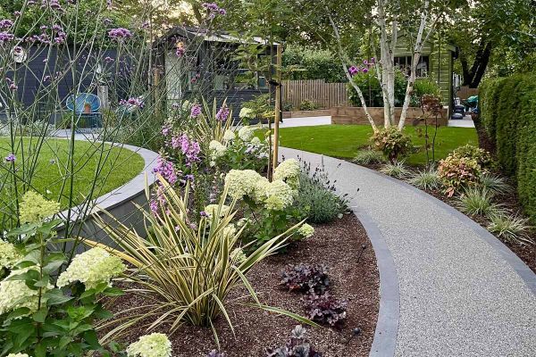 Curved pebble path with platinum grey porcelain setts lining either side runs through flowerbeds and bushes leading to garden shed.***The Landscape Design Studio
