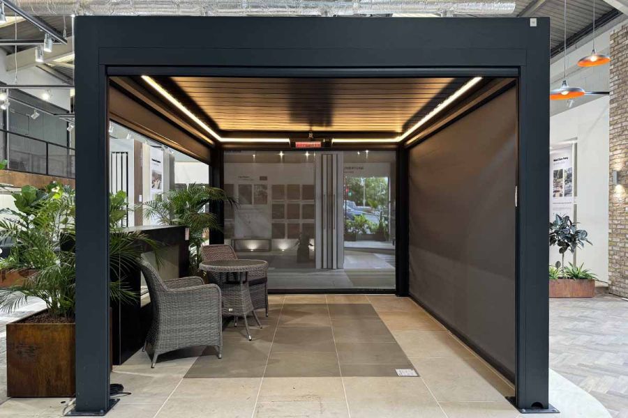 Deluxe Anthracite Grey Metal Pergola in a showroom with the blinds half up half down and integrated lighting and heating on, creating a cosy ambiance.