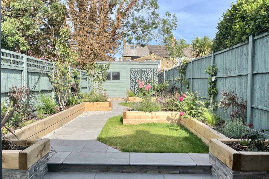 Bullnose outdoor steps lead up to path paved in graphite grey limestone paving, with interspersed lawn and raised flowerbeds.