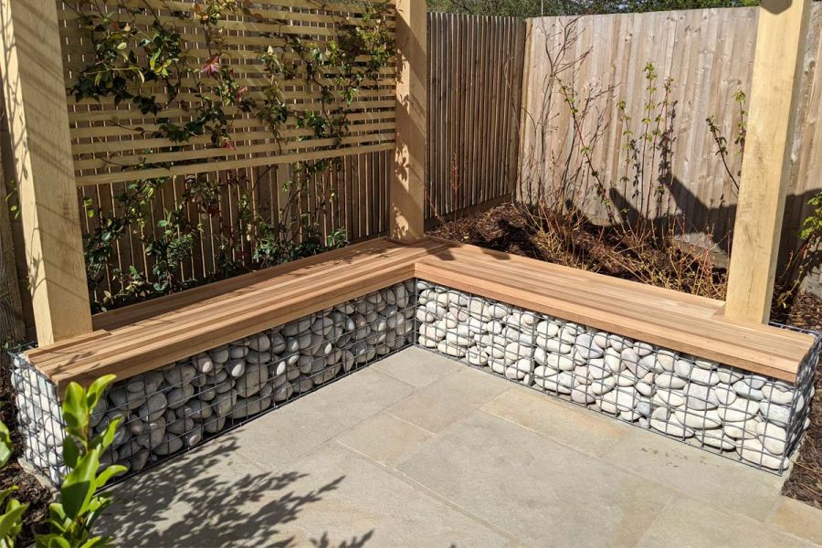 Corner of Antique Yellow limestone patio with bench of wood-topped, stone-filled gabions on 2 sides below wood-batten trellis.