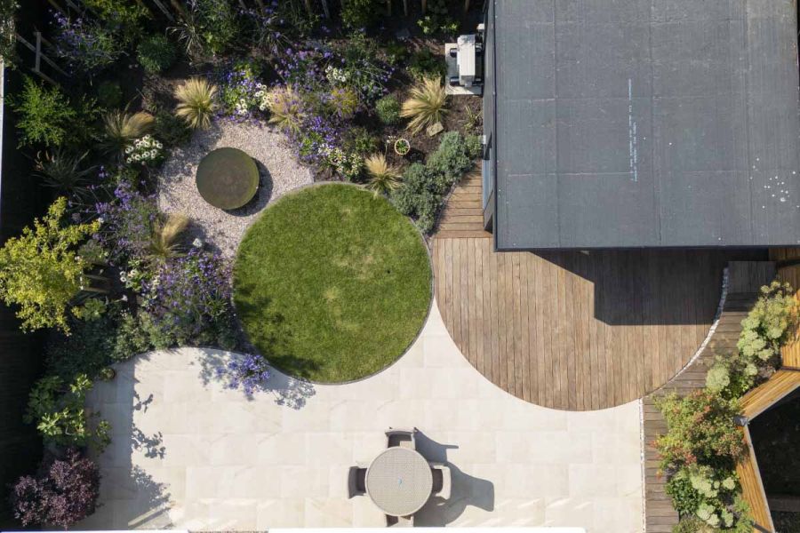 Birds eye view of unique garden design with circular lawn, deck and ash beige porcelain patio paving.