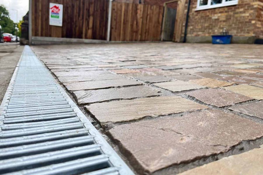 Close up, angled shot of Raj Green Sandstone Cobble Setts used on driveway next to channel drain shows off hand-cut edges.