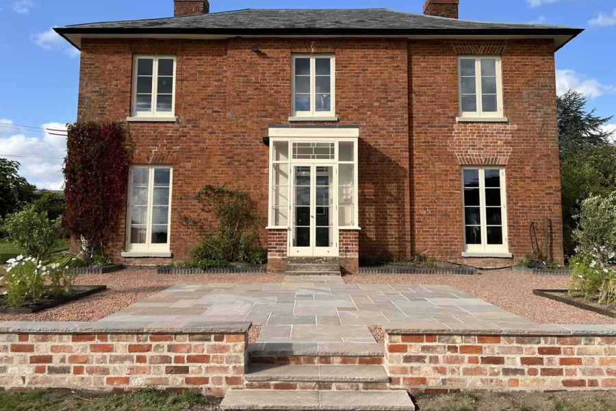 Centred view of traditional house using autumn brown indian sandstone paving, rock-faced copings and steps.