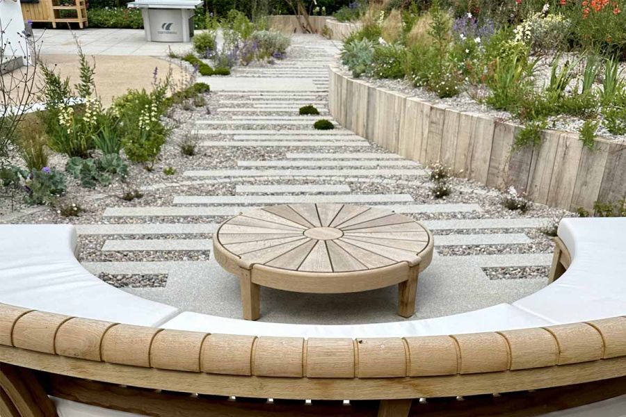 Circular built in bench seen around circle table on granite patio in plank formation, pebbles inbetween the paving.