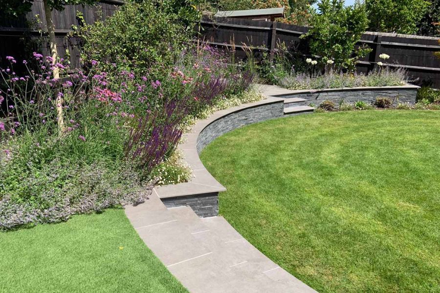 Large circular lawn bordered by curved retaining wall and steps. Walls clad with Black Slate Stone Cladding.