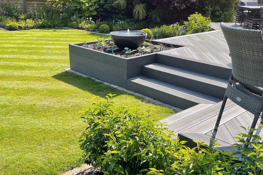 Raised deck with Charcoal composite fascia boards, overlooking a garden with a bowl water feature on a planted bed at the corner edge.