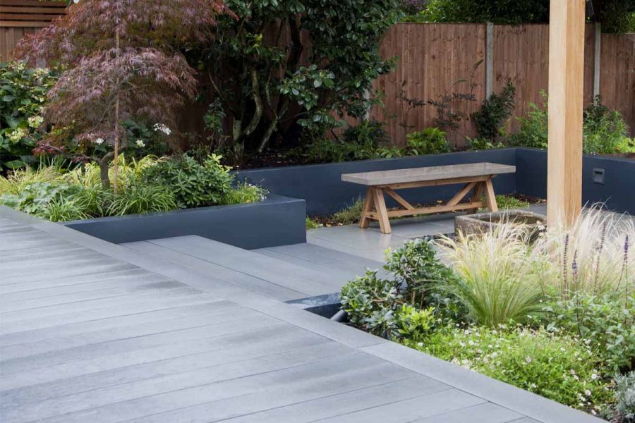 Raised flowerbeds enclose sunken patio with black basalt composite millboard decking used on steps and deck.