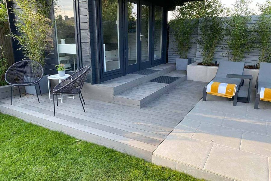 Sunloungers and bistro set on porcelain paving with Pebble Grey Brushed composite fascia boards in front of a glass-fronted garden room.