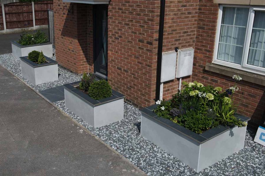 front garden with 3 raised flowerbeds with grey pebbles beneath, charcoal porcelain planks used as coping on the tops.