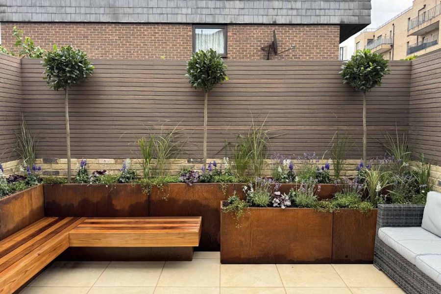 Chestnut Composite battens seen in the distance in front of floating bench, tall trees and stacked corten steel planters.