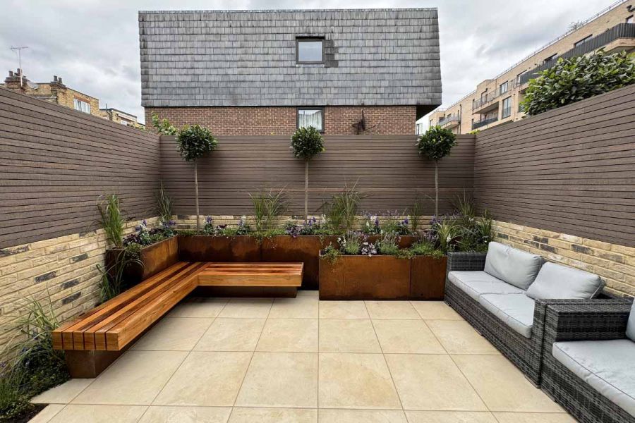 Chestnut composite battens surround garden using porcelain paving on patio with steel corten planter display and floating bench.