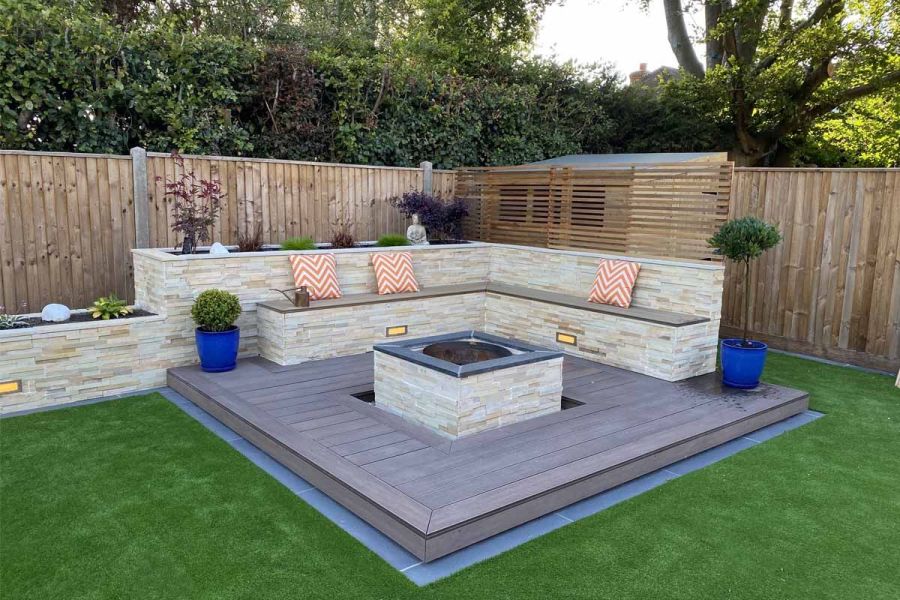 Stone-clad raised bed and bench framed with Chestnut Grooved composite decking and fascia, centered around a firepit with matching cladding.