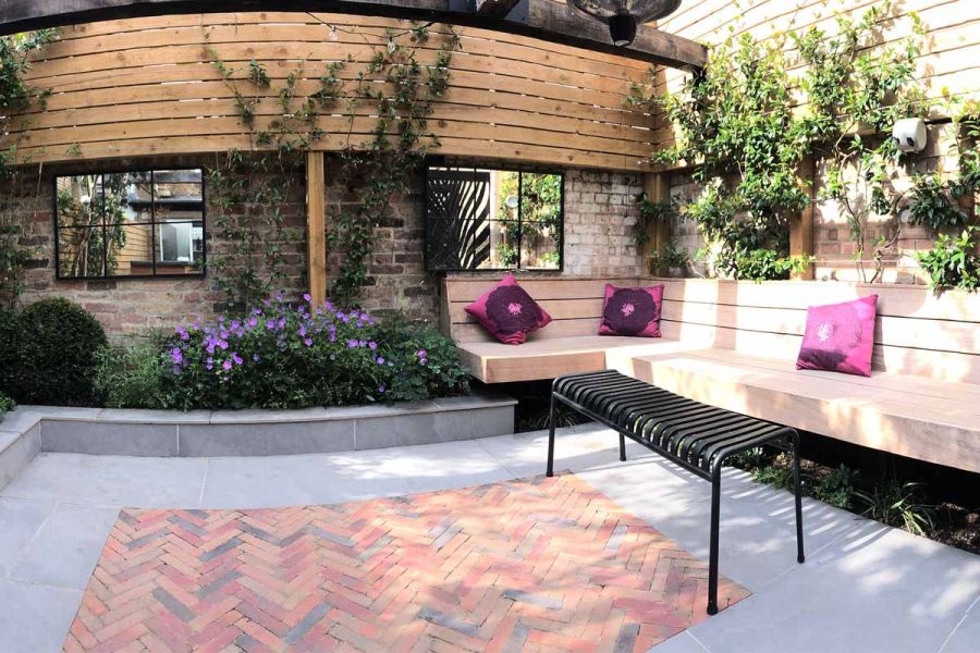 Seville Clay Pavers in a rectangular space bordered by Porcelain Paving, featuring a corner bench with purple cushions in an angled view.