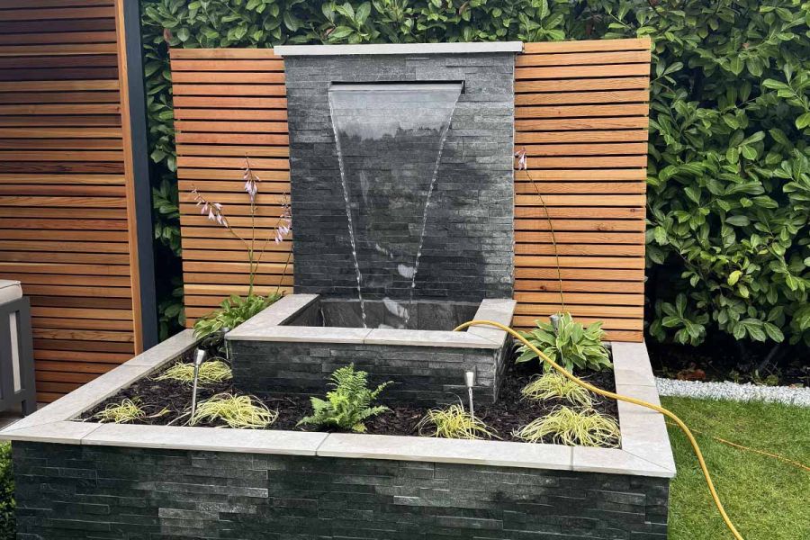 Waterfall feature clad with slate uses comblanchien 5mm chamfered porcelain coping stones on top of rendered walls.