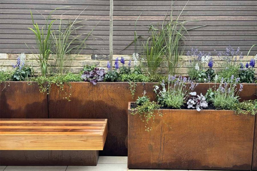 Composite battens in chestnut colour seen in the background, in front are floating bench and corten steel planters.