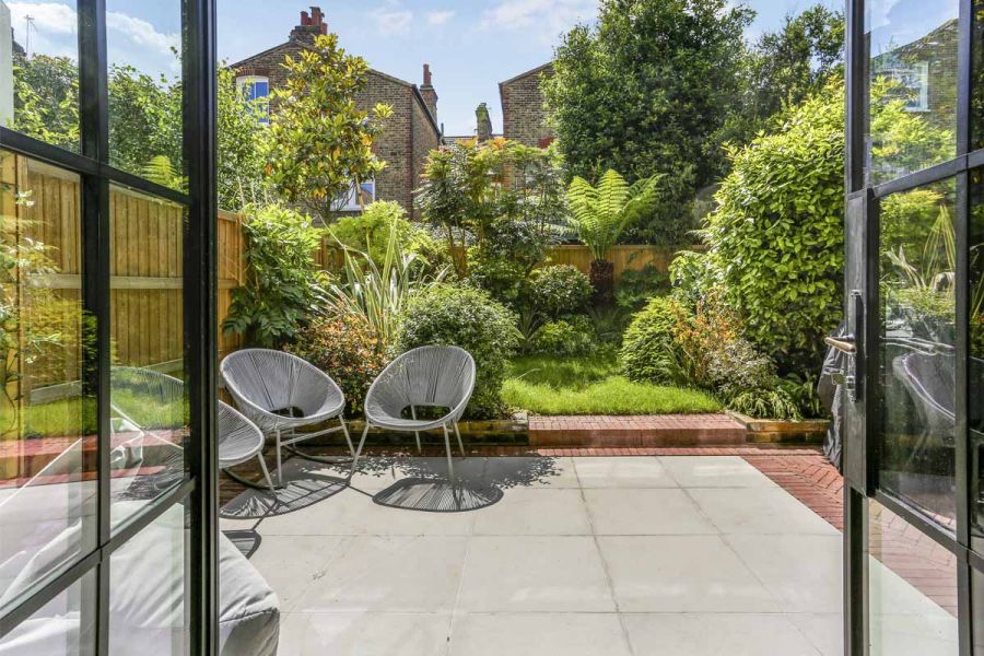 2 chairs on contemporary grey sawn sandstone patio in front of large bushes and trees, view from house.