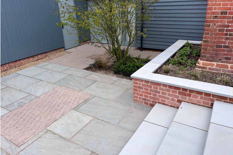Sandstone and clay paver patio flanked by red brick flowerbeds topped with contemporary grey sawn sandstone copings.