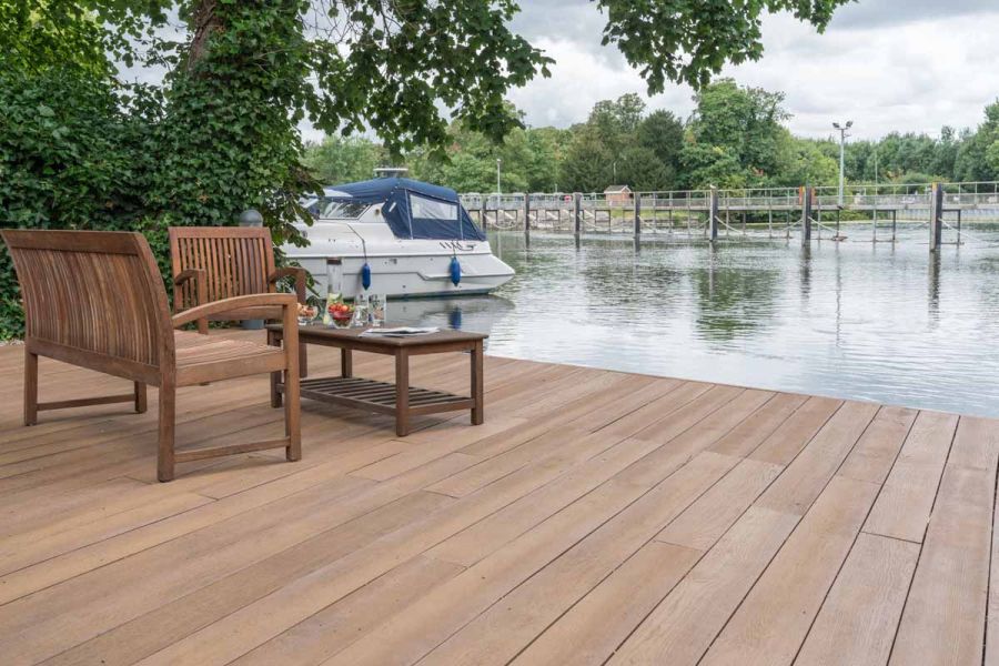 Two wooden benches surround a table on coppered oak millboard decking with views of a River and boat.