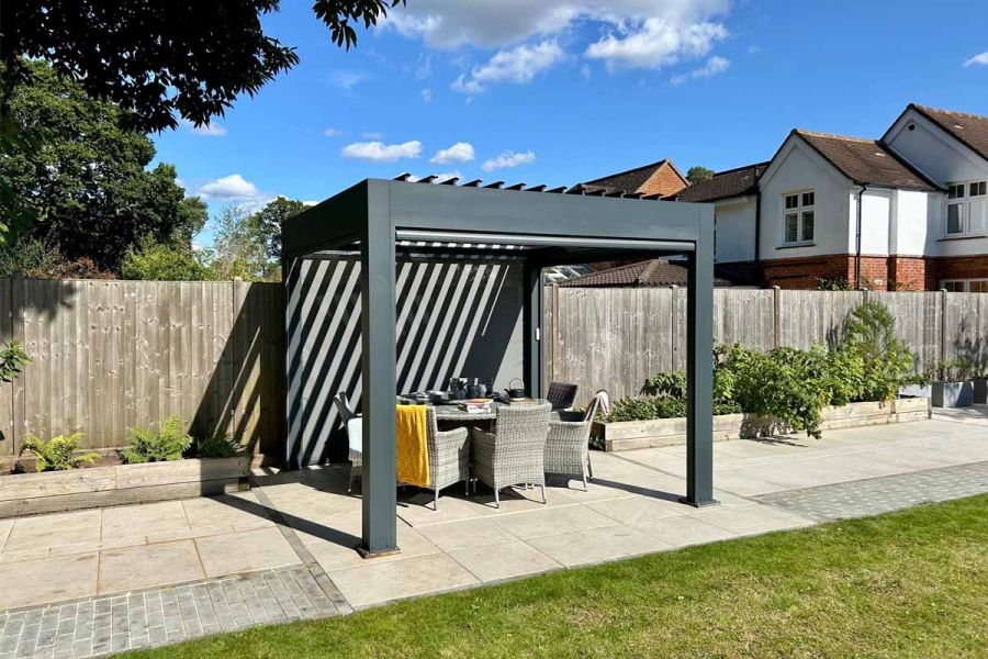 Side angle of the Deluxe Anthracite 3x3 Metal Pergola with louvres open, showing the dining table underneath and blue sky above.