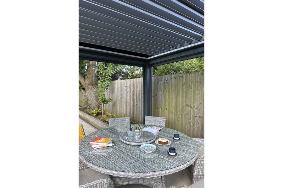 Close-up of the Anthracite Grey 3x3 Deluxe Pergola, showcasing the louvres open and light filtering through the slats onto a dining table.