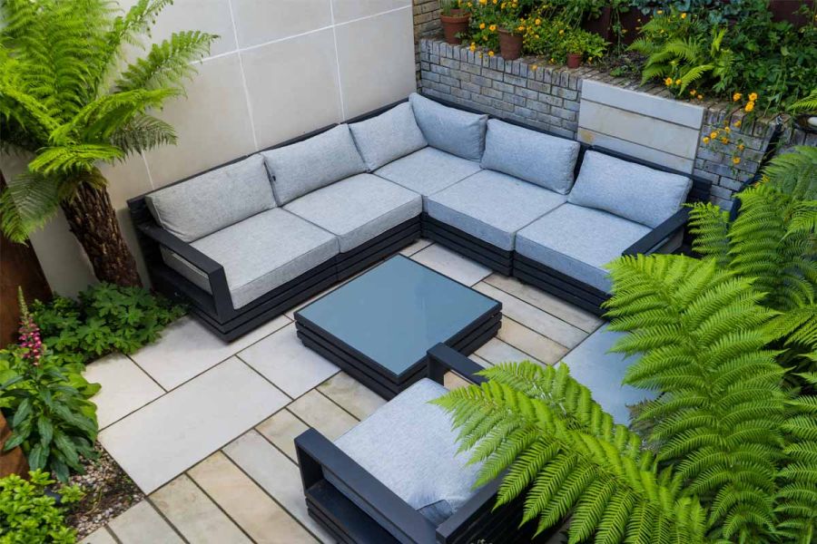 Birds eye view of furniture on Light Grey Porcelain paving slabs around glass table in small garden setting with palm trees.