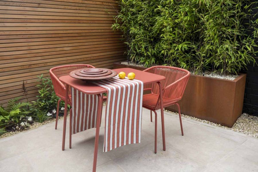 Steel corten planter in background next to red bistro garden furniture sitting on egyptian beige limestone paving.