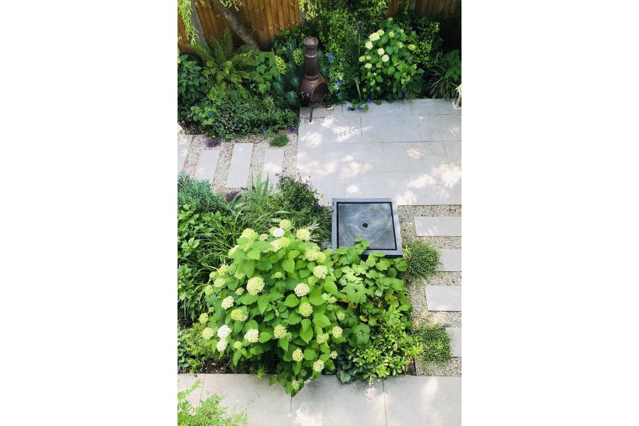 View from above sees Florence Grey Porcelain patio with staggered slabs between pebbles, green plants surrounds with square water feature in the middle.