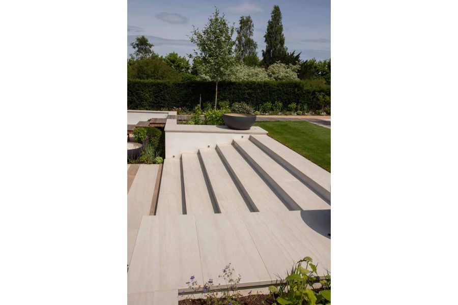 Faro porcelain wall coping stones top wall with steps leading up to a large lawn area, same material used for paving.