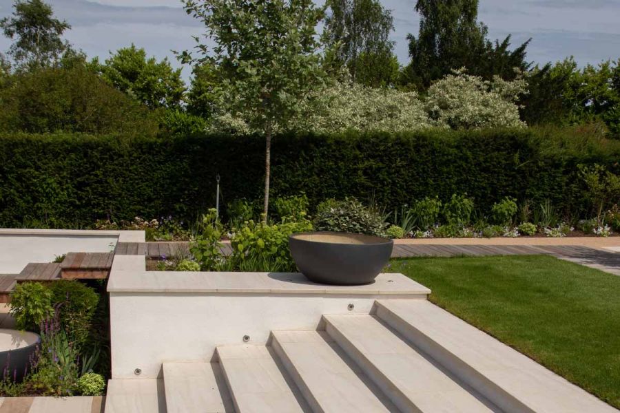 View half-way up a set of Faro Porcelain Steps shows off flat coping stones, large planters and planting and large lawn area.