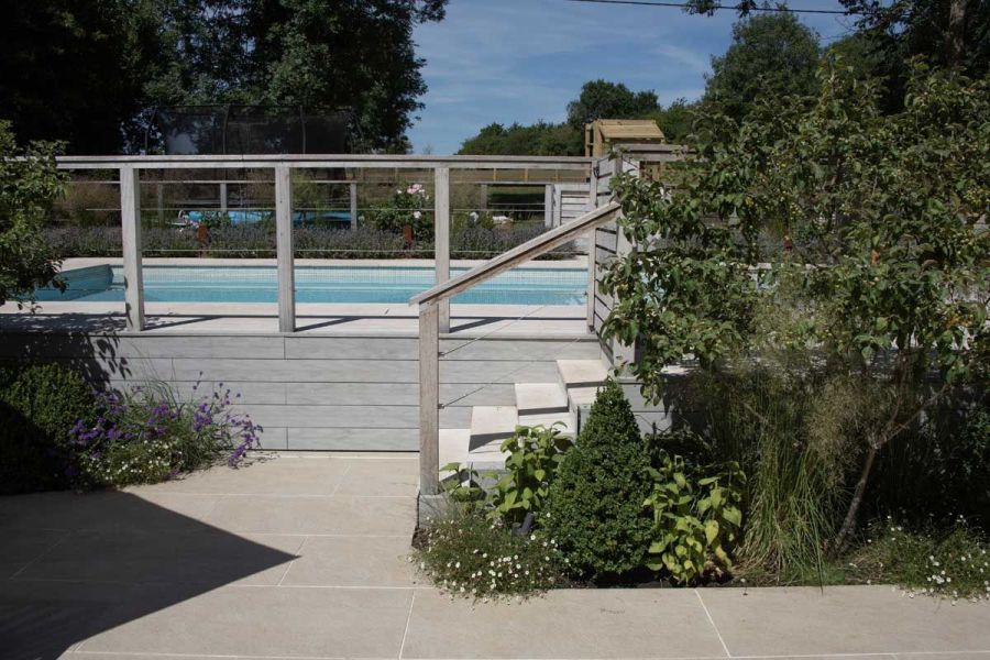 Steps descending from a raised swimming pool, clad in Luna DesignBoard composite fascia boards, leading to a paved area.