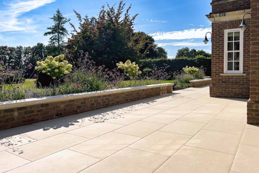 Low view of florence beige porcelain paving on large patio with brick walls separating lawn and paved area.