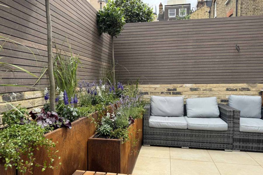 Chestnut Composite battens seen in the background, in front are garden furniture and stacked corten steel planters.