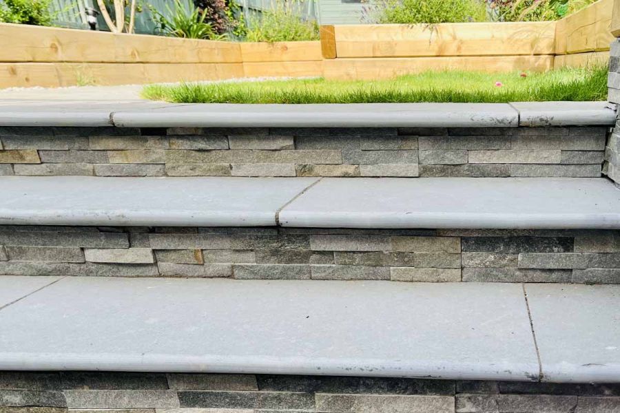 Three graphite grey limestone bullnose outdoor steps lead up to lawn area, clad in graphite sandstone cladding.