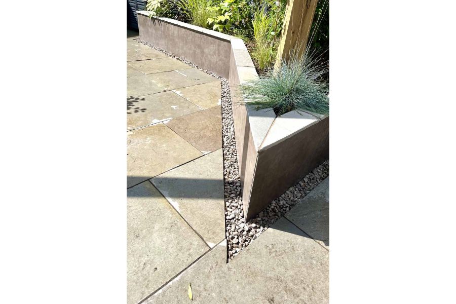 Sharp angled raised flowerbed with porcelain cladding sits next to graphite grey limestone paving.