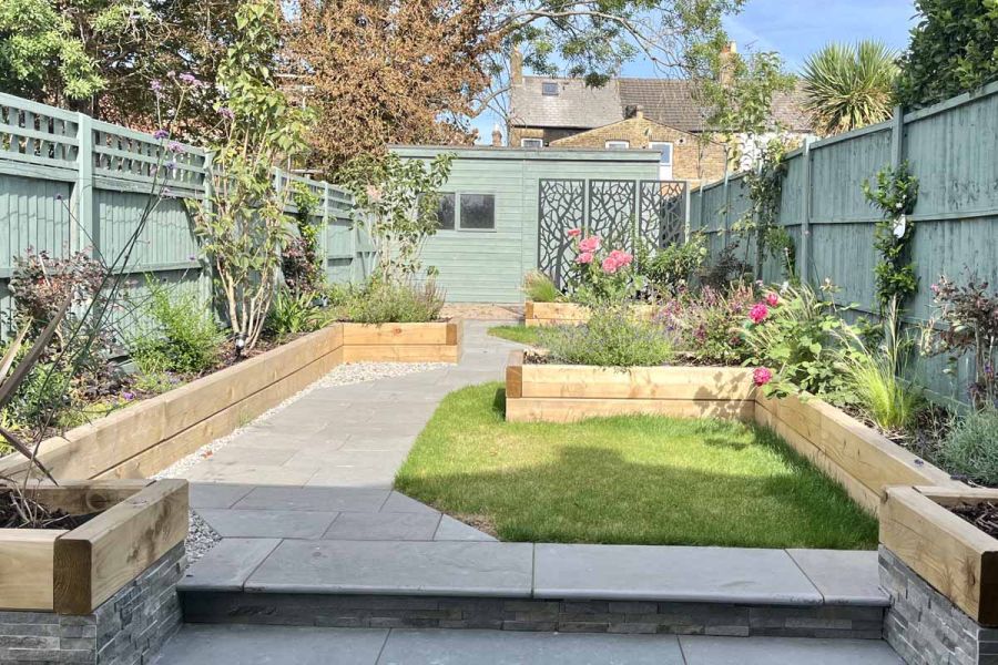 Bullnose steps lead up to path paved in graphite grey limestone paving, with interspersed lawn and raised flowerbeds.