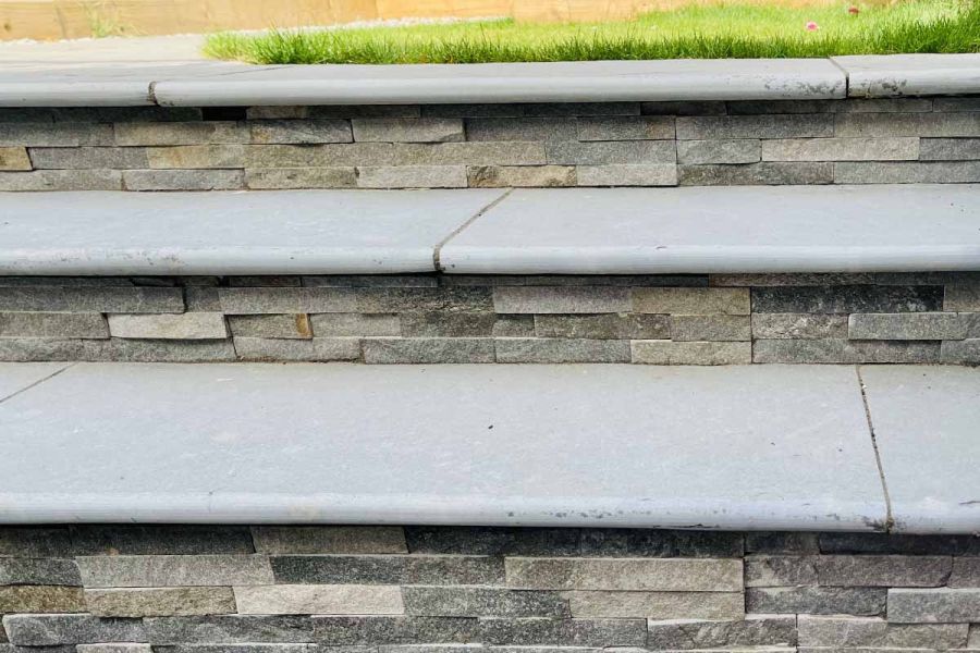 Three graphite grey limestone bullnose steps lead up to lawn area, clad in graphite sandstone external cladding.