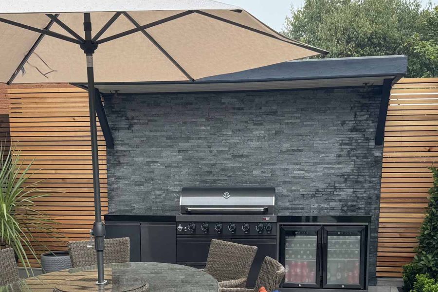 Umbrella seen in foreground, green slate cladding used as splashback and feature wall on outdoor cooking area.