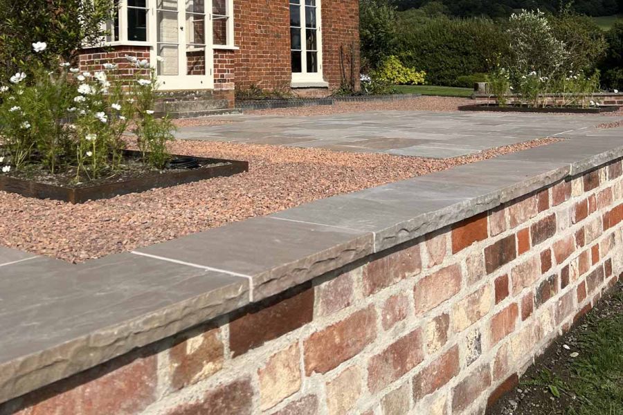 Close up of Autumn Brown Indian Sandstone Copings rock-faced edges, used on red brick wall with white grouting.