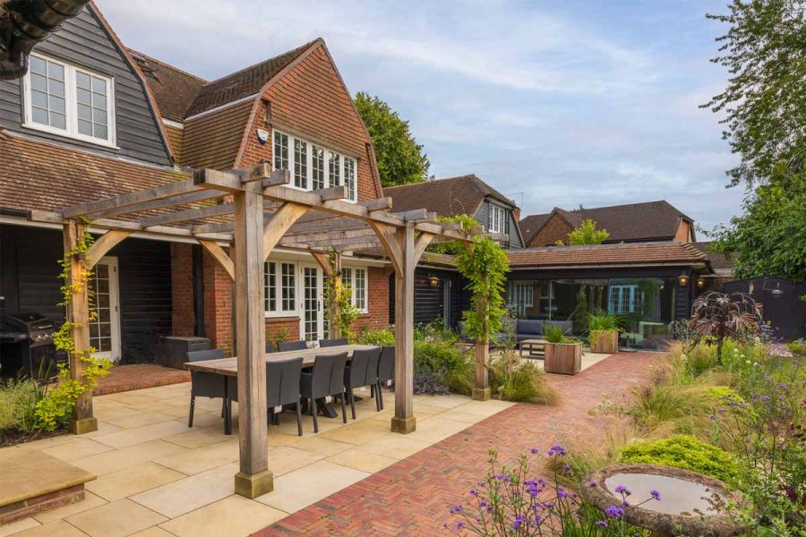 Wooden pergola sits on harvest sawn sandstone patio with clay paver path making a break between patio and lawn.