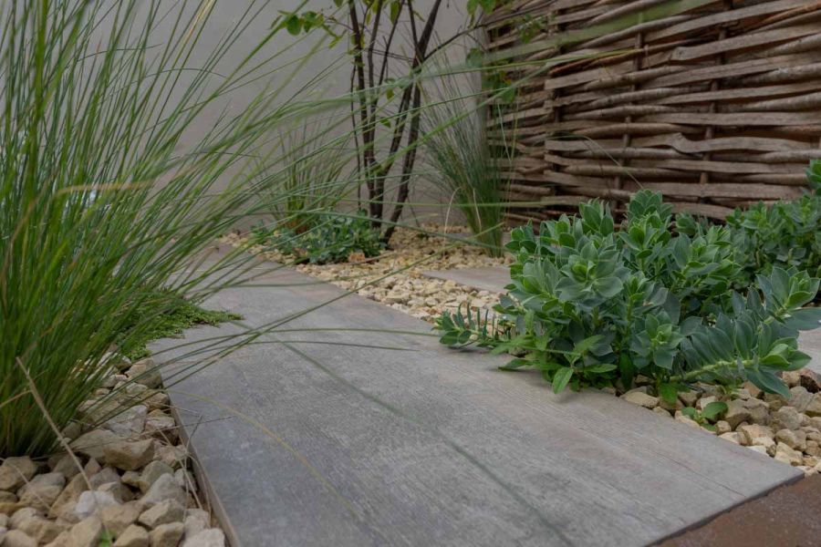 Low angle shot of cinder porcelain paving showing off its wood like effect, plants and pebbles either side.