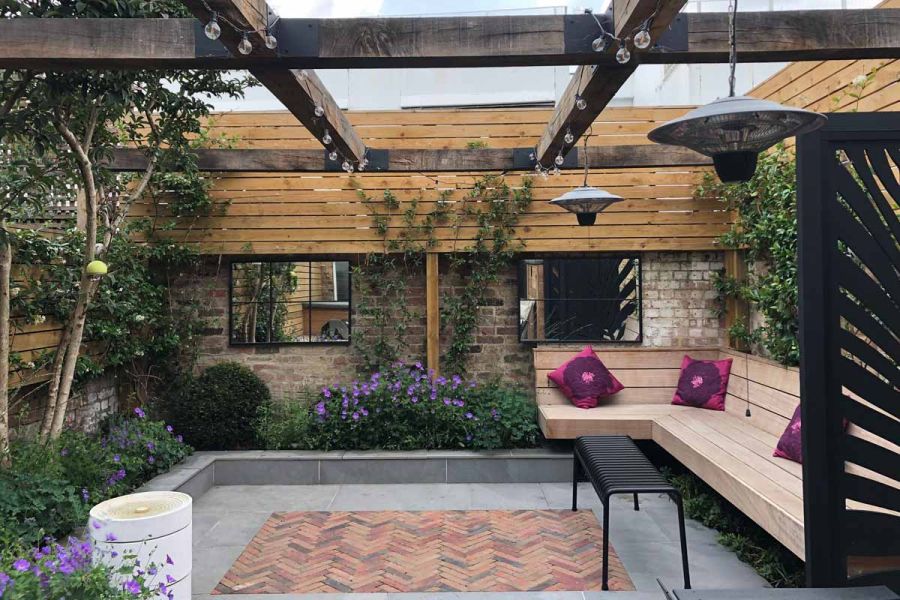Seville Clay Pavers and Porcelain Paving in a garden with mirrors on the brick walls, a wooden pergola, and lush planting.