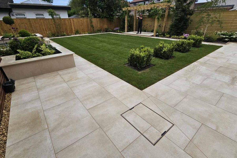 A well-manicured rectangular lawn with four neatly planted bushes is surrounded by a cream porcelain paving patio.