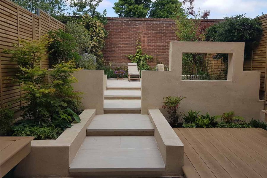 Golden Oak Millboard decking to right of faro porcelain patio area with wide steps leading to sunlounger. 