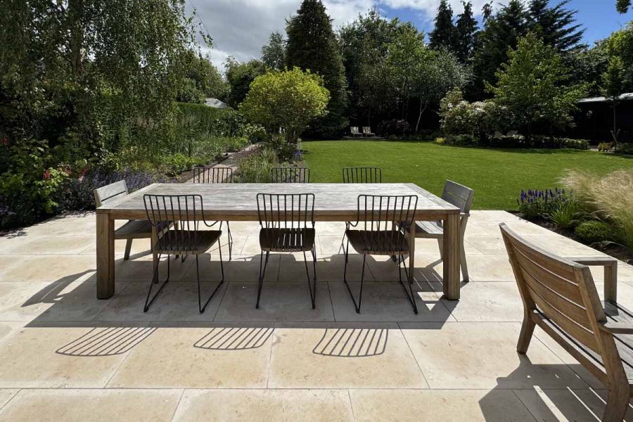 Wooden dining table and chairs sit on jura beige limestone patio with views overlooking a well manicured lawn.