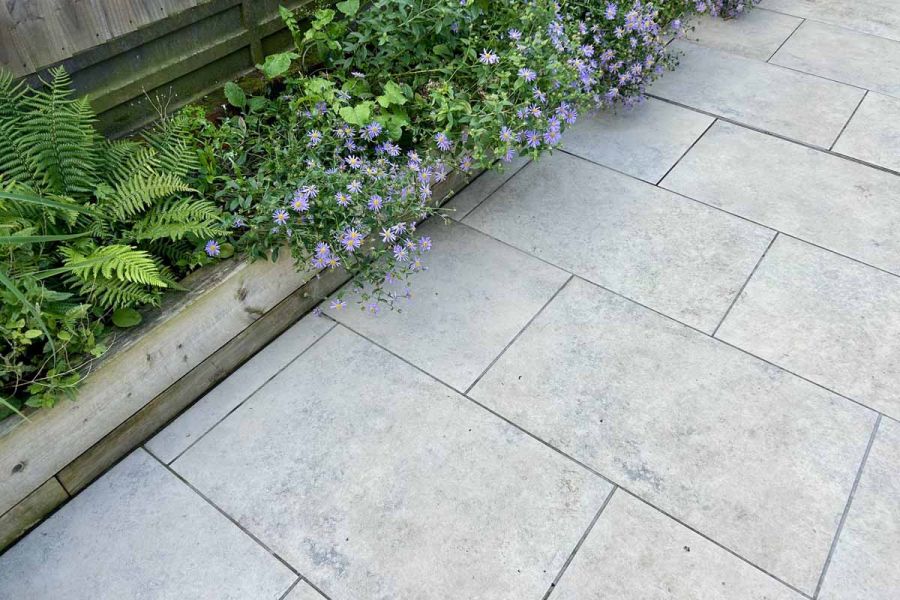 Built in flowerbeds run alongside jura grey porcelain paving in close up view showing tones and textures of this stone-inspired porcelain.