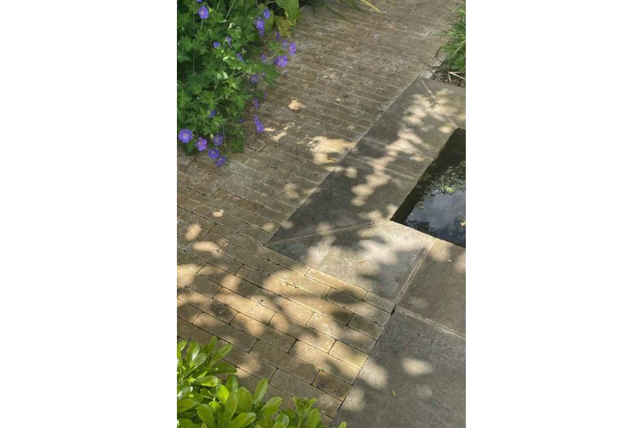 Shadows cast over westminster clay paver bricks and raj green sandstone with foliage surrounding a water feature.