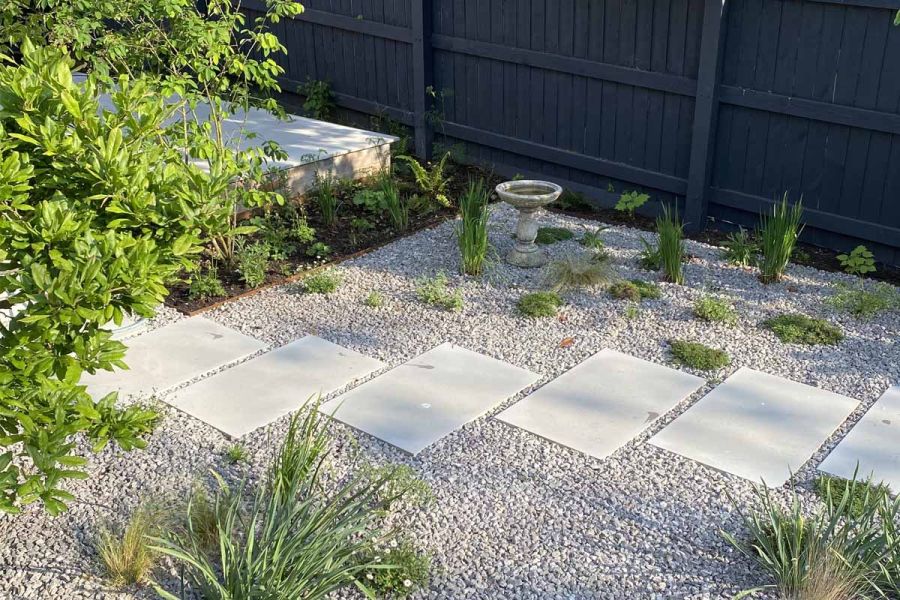Stepping stones created with Dove Grey Sawn Sandstone Paving create path through pebbles and green foliage.