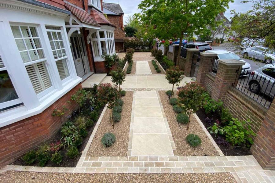 Cross-shaped path using Harvest Smooth Sandstone paving and tumbled setts surrounded by pebbles and lined with bushes lead to front door.